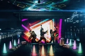 ネオンライトと幾何学的な模様が輝くステージでパフォーマンスを行う3人のパフォーマー