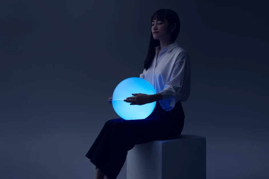 青く光る球体型のサウンドハグを抱きかかえる女性